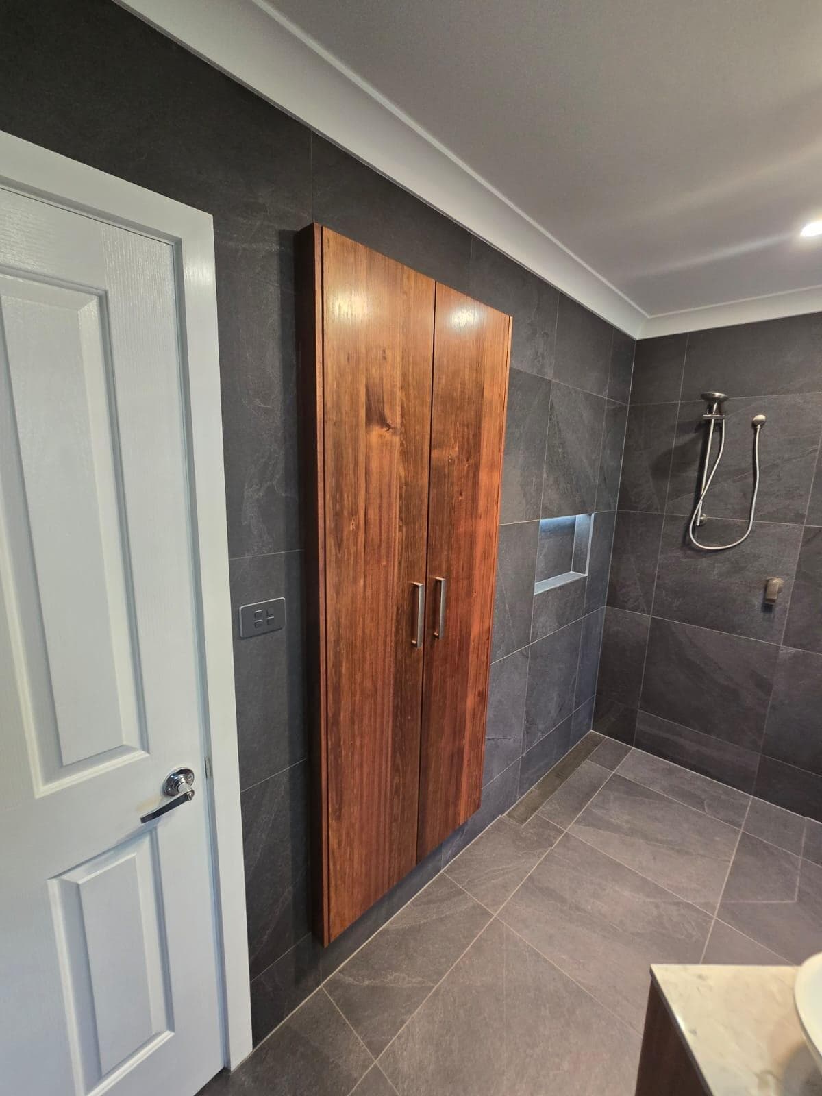 Modern bathroom renovation in Canberra, Australia with dark slate tiles and timber cabinetry.