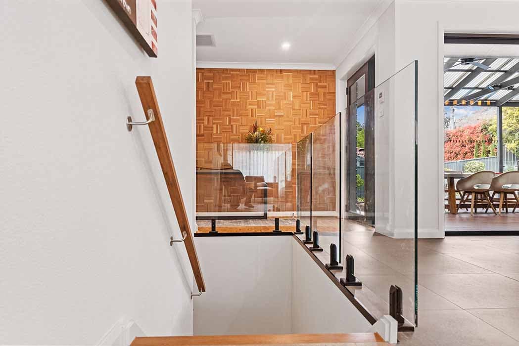 Modern staircase renovation in Canberra, Australia with glass balustrade and wood accents.