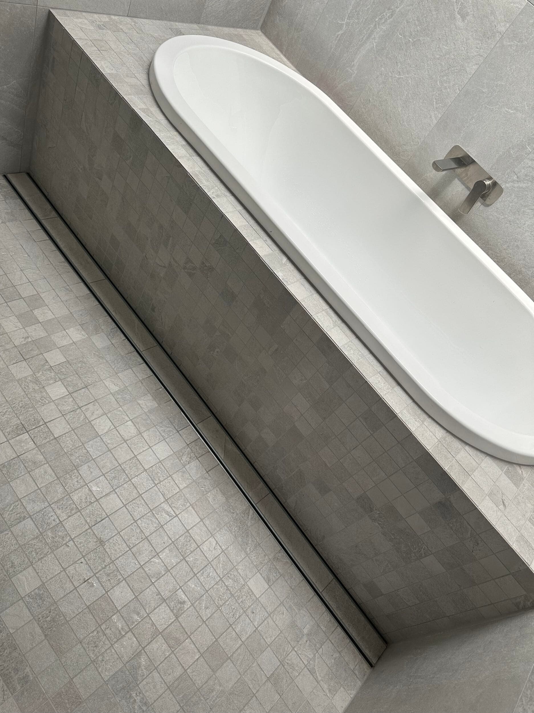 Modern bathroom renovation in Canberra with elegant grey tiles and freestanding bathtub.